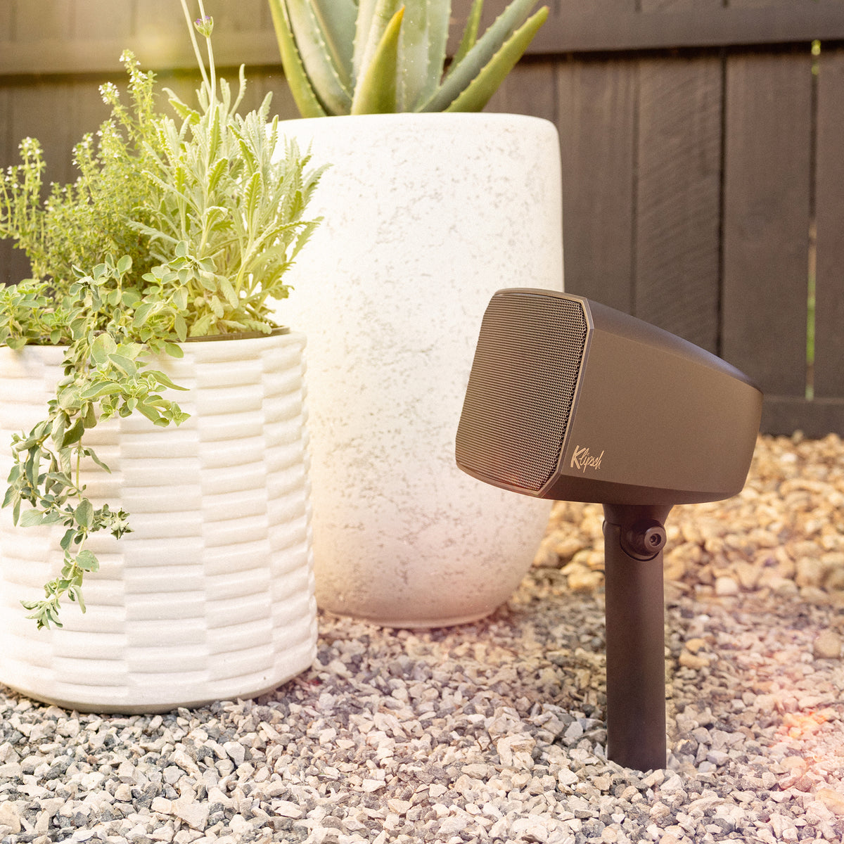 Klipsch Courtyard 2.0 Black Klipsch Courtyard Speaker outdoors in gravel beside stylish white planters 2000x2000